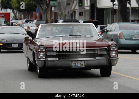 Una classica cabriolet rossa Cadillac rotola lungo una strada della città con i passeggeri che lampeggiano segnali di pace, incarnando un'atmosfera rilassata e vintage. Foto Stock