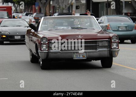 Una classica cabriolet rossa Cadillac rotola lungo una strada della città con i passeggeri che lampeggiano segnali di pace, incarnando un'atmosfera rilassata e vintage. Foto Stock