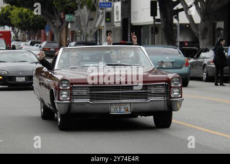 Una classica cabriolet rossa Cadillac rotola lungo una strada della città con i passeggeri che lampeggiano segnali di pace, incarnando un'atmosfera rilassata e vintage. Foto Stock