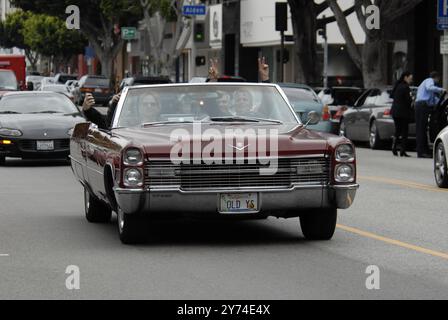 Una classica cabriolet rossa Cadillac rotola lungo una strada della città con i passeggeri che lampeggiano segnali di pace, incarnando un'atmosfera rilassata e vintage. Foto Stock