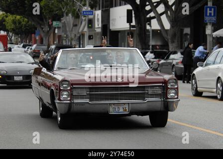 Una classica cabriolet rossa Cadillac rotola lungo una strada della città con i passeggeri che lampeggiano segnali di pace, incarnando un'atmosfera rilassata e vintage. Foto Stock