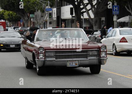 Una classica cabriolet rossa Cadillac rotola lungo una strada della città con i passeggeri che lampeggiano segnali di pace, incarnando un'atmosfera rilassata e vintage. Foto Stock