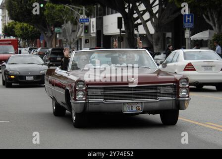 Una classica cabriolet rossa Cadillac rotola lungo una strada della città con i passeggeri che lampeggiano segnali di pace, incarnando un'atmosfera rilassata e vintage. Foto Stock