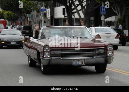 Una classica cabriolet rossa Cadillac rotola lungo una strada della città con i passeggeri che lampeggiano segnali di pace, incarnando un'atmosfera rilassata e vintage. Foto Stock