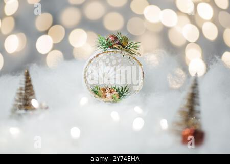 Concetto di deorazione natalizia durante le vacanze con un bambino Gesù, neve bianca finta per un dicembre festivo. Sullo sfondo ci sono palline bokeh fatte di luci Foto Stock