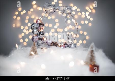 Concetto di deorazione natalizia durante le vacanze con derr d'argento, neve finta bianca per le festività di dicembre. Sullo sfondo ci sono palline bokeh fatte di luci Foto Stock