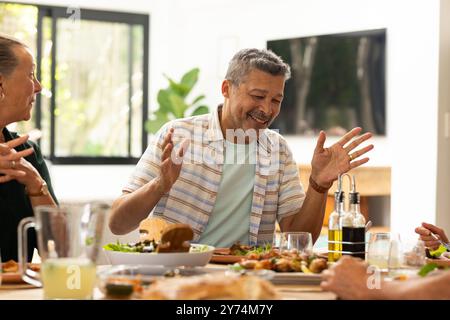 Gustati un pasto, amici anziani che ridono e parlano intorno al tavolo da pranzo, a casa Foto Stock