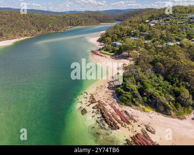 Vista aerea dell'oceano turchese intorno a un fiume che scorre oltre le spiagge sabbiose di Pambula Beach nel New Southern Wales, Australia. Foto Stock