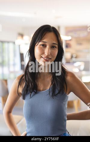 Donna sorridente con canotta blu che posa con sicurezza in un ambiente casual al chiuso, a casa Foto Stock