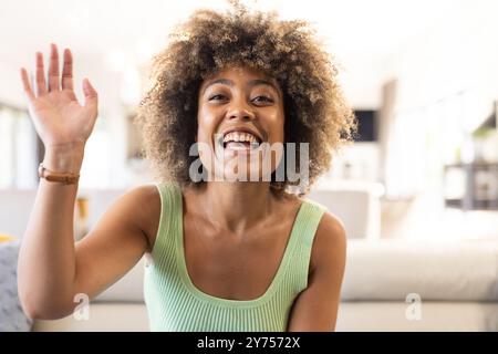 In videochiamata, donna sorridente che sventola la mano, a casa Foto Stock