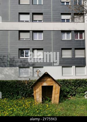 Una casa per cani in legno annidata in un'area erbosa accanto ad un moderno edificio di appartamenti durante il giorno Foto Stock