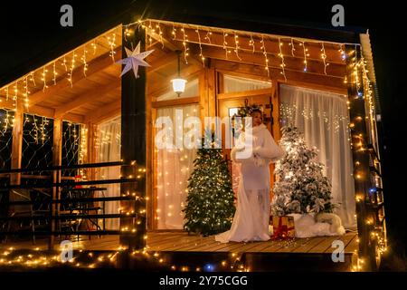 Gravidanza, Natale, servizio fotografico: Una donna incinta posa di fronte a una cabina decorata durante un servizio fotografico festivo. Foto Stock