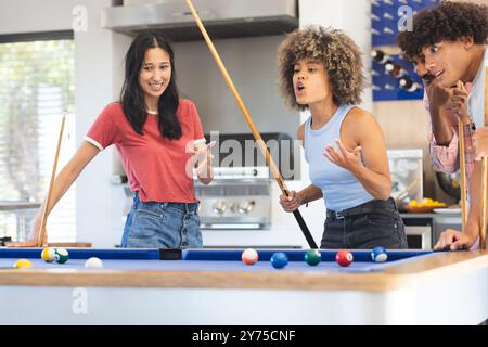 Giocare a biliardo, amici diversi che si divertono e socializzano intorno al tavolo da biliardo, a casa Foto Stock