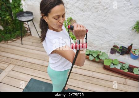 Una donna si impegna in un esercizio di forza utilizzando una fascia di resistenza nel suo patio all'aperto, incarnando uno stile di vita attivo e in forma. Foto Stock