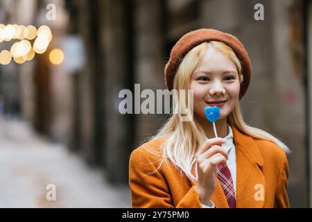 Giovane donna sorridente e con in mano un lecca lecca a forma di cuore blu a barcellona Foto Stock