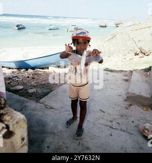 Kleines Mädchen zeigt einen 'Fliegenden Fisch' (Exocoetidae) auf dem Fischmarkt in Bridgetown auf Barbados, um 1985. Foto Stock