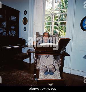 Ein Reisender Hat Platz genommen in einem hochinteressanten Multifunktionssessel mit Beinstüze, Arbeitstisch, Getränkehalter und Leselampe. Dieser befindet siich im Saint Nicholas Abbey Herrenhaus in Saint Peter auf Barbados, um 1985. Foto Stock