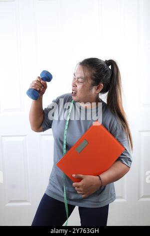 Donna asiatica che tiene Dumbell, Scale, and Measuring Tape, Sad Emotion, Diet Concept Foto Stock