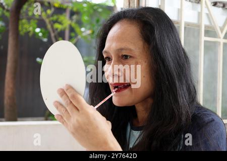 Donna di mezzo asiatica che applica il rossetto rosso e tiene uno specchio Foto Stock