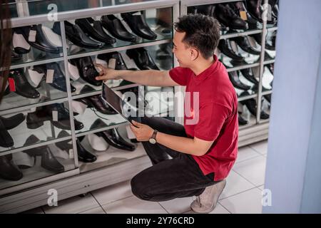 dipendente asiatico che lavora in un negozio di scarpe in pelle utilizzando un tablet Foto Stock