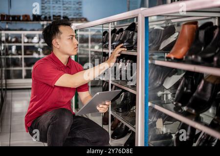 venditore asiatico che tiene un tablet per lavorare in un negozio di scarpe in pelle Foto Stock