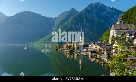 Annidato tra vette torreggianti, un pittoresco villaggio sul lago riflette il cielo azzurro Foto Stock