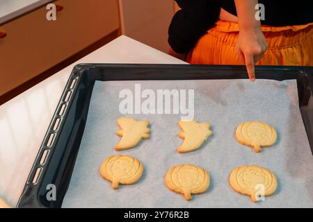 Una persona sta indicando un vassoio di biscotti di Halloween. I biscotti sono decorati con forme di zucca e fantasma Foto Stock