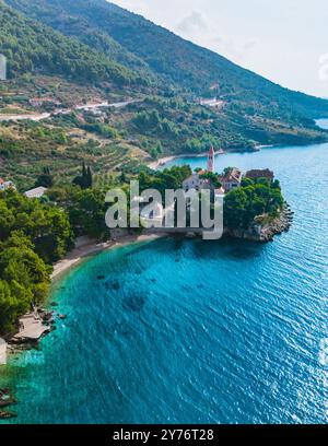 Sull'isola di Brac in Croazia, le acque cristalline turchesi si adagano dolcemente sulla riva, incorniciate da una vegetazione lussureggiante e da pittoresche colline. Il tranquillo paesaggio invita al relax e all'esplorazione. Foto Stock