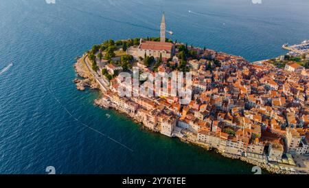 Il sole tramonta su Rovigno, proiettando un bagliore dorato sui tetti colorati e sugli antichi edifici, mentre l'Adriatico lambisce dolcemente sulla riva, creando un'atmosfera serena in questa città costiera. Foto Stock