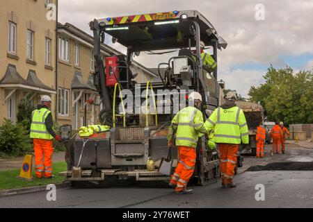 Un team di operai che gestiscono macchinari pesanti per ripavimentare una strada residenziale nel Wiltshire. Foto Stock