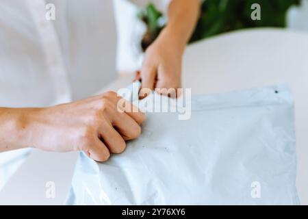 mani di una giovane donna che disimballa un sacchetto di plastica, acquista merci online, Foto Stock