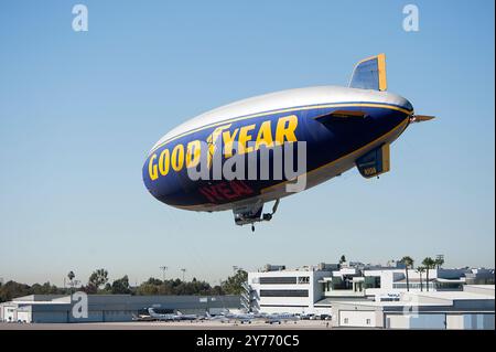 L'iconico Goodyear Blimp, simbolo dell'aviazione dirigibile, vola agevolmente sopra un aeroporto. Catturato contro un cielo limpido con vista degli hangar sottostanti Foto Stock