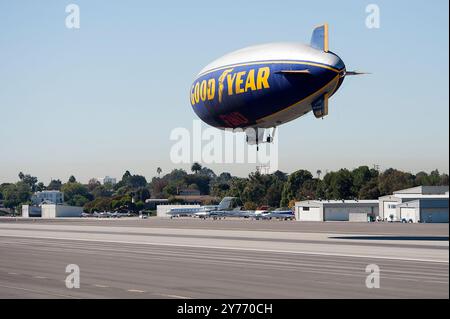 L'iconico Goodyear Blimp, simbolo dell'aviazione dirigibile, vola agevolmente sopra un aeroporto. Catturato contro un cielo limpido con vista degli hangar sottostanti Foto Stock