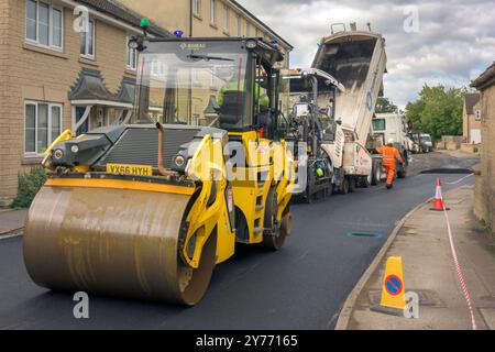 Un team di operai che gestiscono macchinari pesanti per ripavimentare una strada residenziale nel Wiltshire. Foto Stock