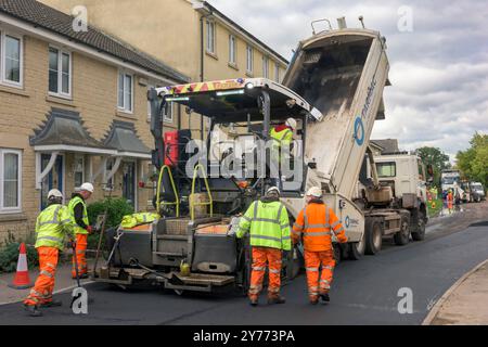 Un team di operai che gestiscono macchinari pesanti per ripavimentare una strada residenziale nel Wiltshire. Foto Stock