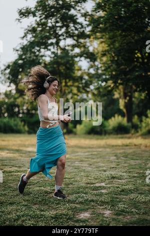 Donna gioiosa che balla nel parco ascoltando musica con le cuffie Foto Stock