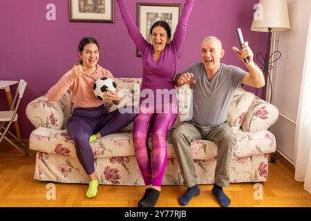 Famiglia di tifosi che si divertono a guardare la partita di calcio in TV a casa. Un uomo emotivo e una ragazza adolescente che esultano la loro squadra preferita, l'entusiasmo della famiglia Foto Stock