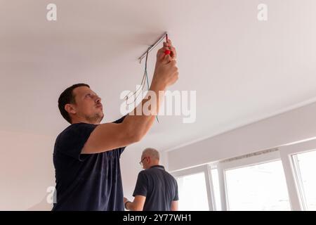 Installazione di una plafoniera a LED. Le mani di un elettricista stanno installando e collegando una lampada a soffitto. Restauro in spazi chiusi. Foto Stock