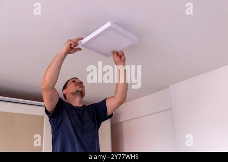 Installazione di una plafoniera a LED. Le mani di un elettricista stanno installando e collegando una lampada a soffitto. Restauro in spazi chiusi. Foto Stock