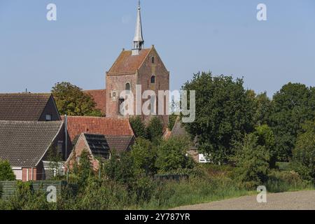 Una chiesa in mattoni sovrasta un piccolo villaggio e un paesaggio verde sotto un cielo azzurro, Greetsiel, Frisia orientale, Germania, Europa Foto Stock