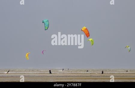 Diversi aquiloni colorati che si aggirano sulla spiaggia mentre la gente fa kite surf, Sankt Peter Ording, Schleswig Holstein, Germania, Europa Foto Stock