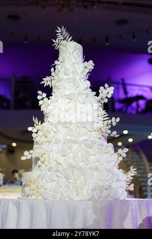 Una torta nuziale bianca a più livelli splendidamente decorata, decorata con intricati motivi floreali, su sfondo viola. Foto Stock