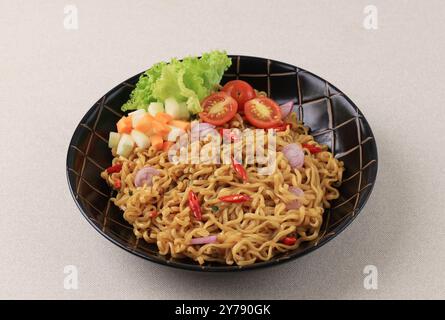 Indomie Goreng piccante, popolare spaghetti istantanei indonesiani con lattuga e pomodoro Foto Stock