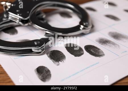 Foglio di carta con impronte e manette umane sul tavolo, primo piano. Condanna penale Foto Stock