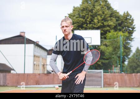 Il giocatore di badminton colpisce il rubinetto durante una partita su un campo all'aperto, mostrando una tecnica precisa e un movimento atletico. Il giocatore è concentrato, Foto Stock