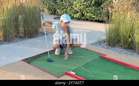 Mini golf - ragazza che gioca a golf su erba verde al tramonto Foto Stock