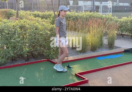 Mini golf - ragazza che gioca a golf su erba verde al tramonto Foto Stock