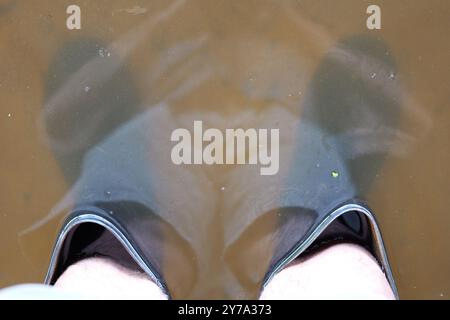 Piedi in stivali quasi sommersi in acqua sporca, riflettendo livelli elevati di inondazione, sfide affrontate durante la situazione delle inondazioni Foto Stock