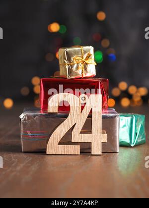 Il ventiquattresimo dicembre è in legno il ventiquattresimo numero con scatole regalo di Natale impilate su uno sfondo sfocato di luci natalizie Foto Stock