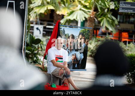 Cairns, Australia. 29 settembre 2024. Un uomo che indossa una maglietta "Palestina libera” siede davanti a un'immagine raffigurante le vittime di uno sciopero israeliano in Palestina durante una manifestazione di solidarietà con la Palestina all'Esplanade di Cairns. I manifestanti si sono riuniti all'Esplanade di Cairns per protestare come parte di una giornata nazionale d'azione a sostegno della Palestina, chiedendo un cessate il fuoco totale e che il governo australiano sancisca Israele. Credito: SOPA Images Limited/Alamy Live News Foto Stock